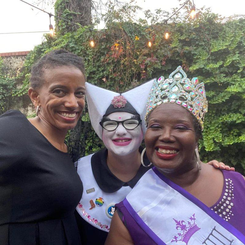 Three Krewe members in crowns and sashes in a courtyard at dusk