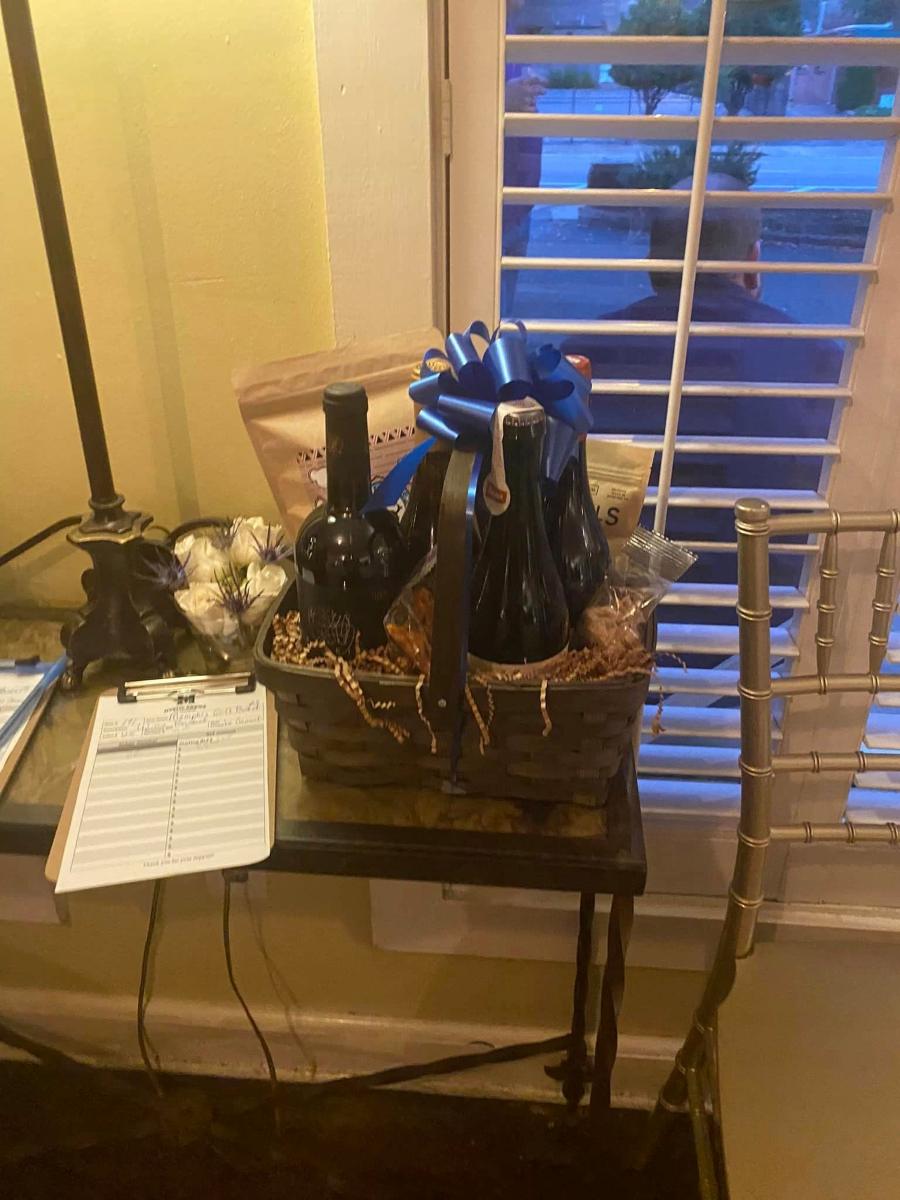 A wine bottle tied with a large blue bow standing on a table beside a bid sheet.