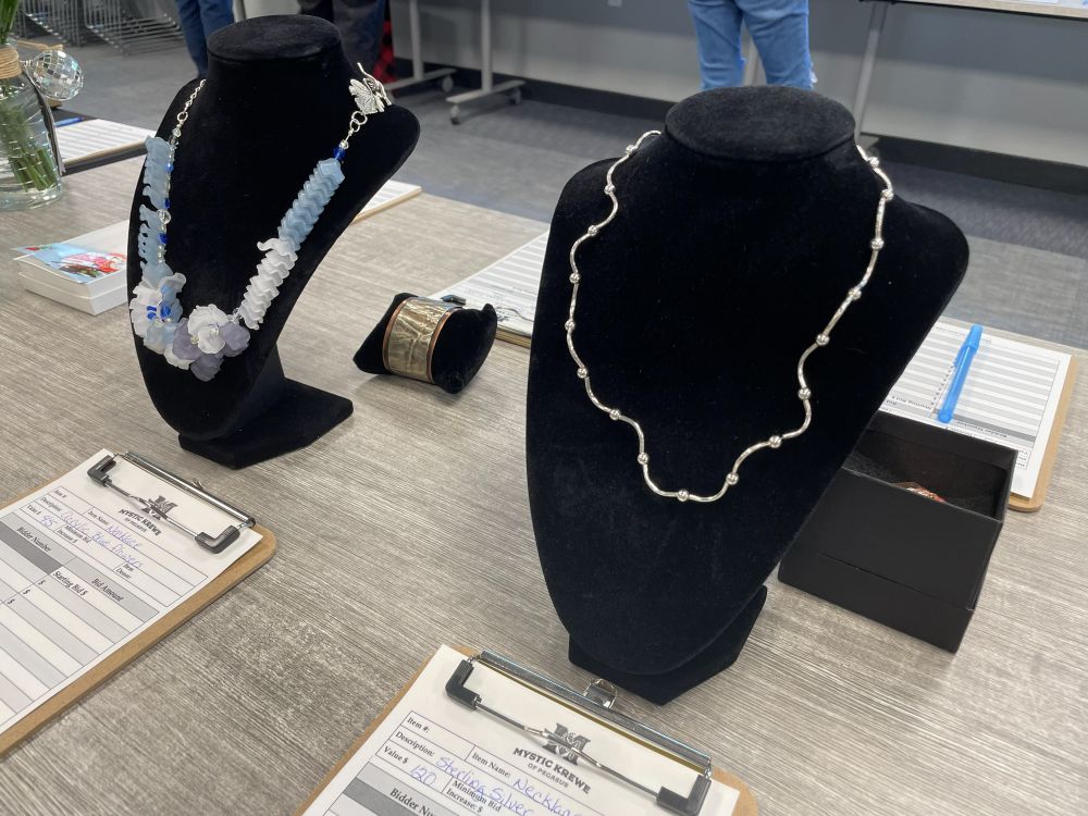 Two necklaces on black velvet busts beside clipboard bid sheets.