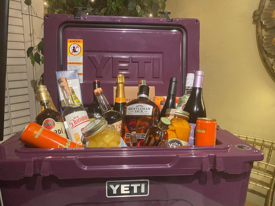 A purple hard cooler packed with bottles of liquor, mixers and snacks as an auction lot.
