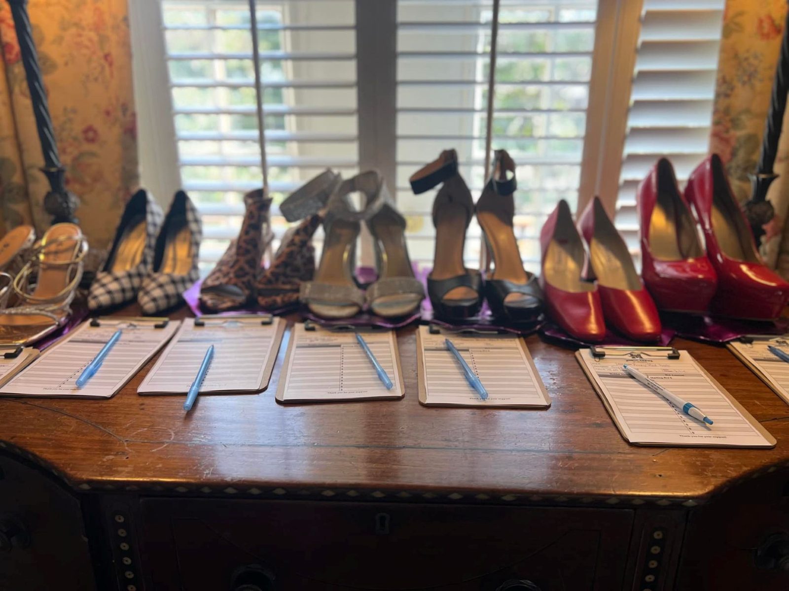A row of designer heels on a sideboard, each pair with its own clipboard bid sheet.