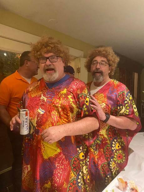 Two guests in curly wigs and bright shirts, laughing.
