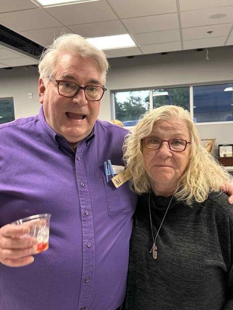 A Krewe member in purple laughing with his arm around a friend.
